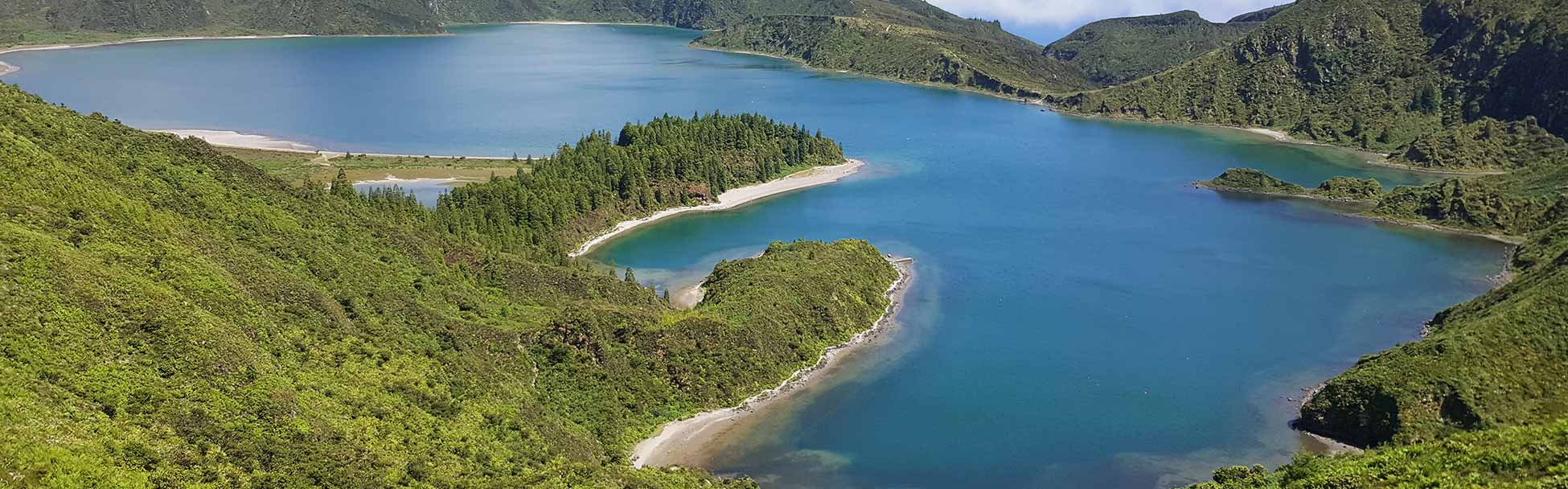 Paisaje de un lago con agua azul rodeado de montes verdes.