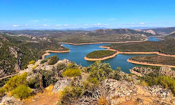 Embalse de agua azul rodeado de arboles y sierras.