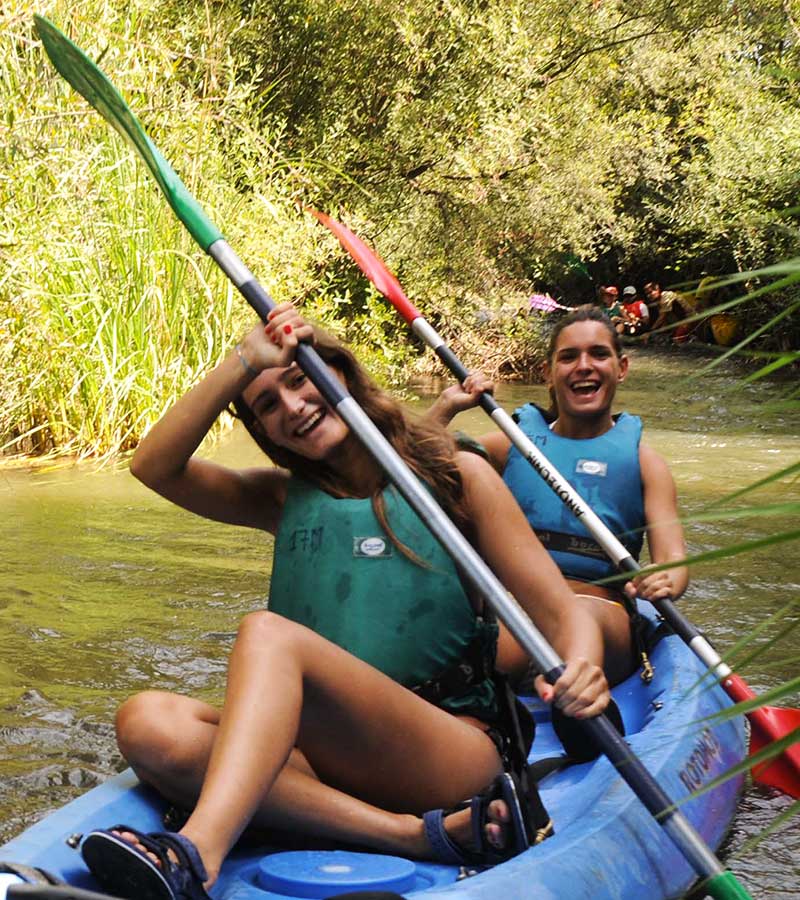 Dos chicas sonrientes navegando juntas en un kayak en un rio.