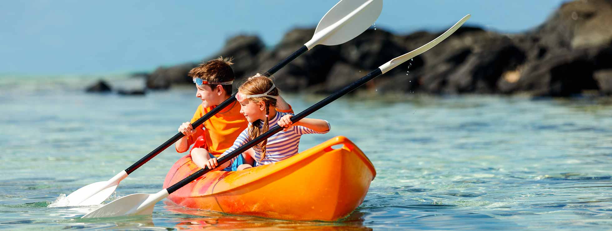 Una niña y un niño remando juntos en una kayak por el mar.