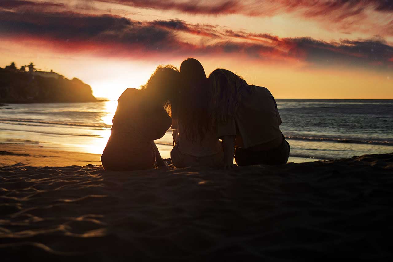 Tres mujeres sentadas en la playa al atardecer.